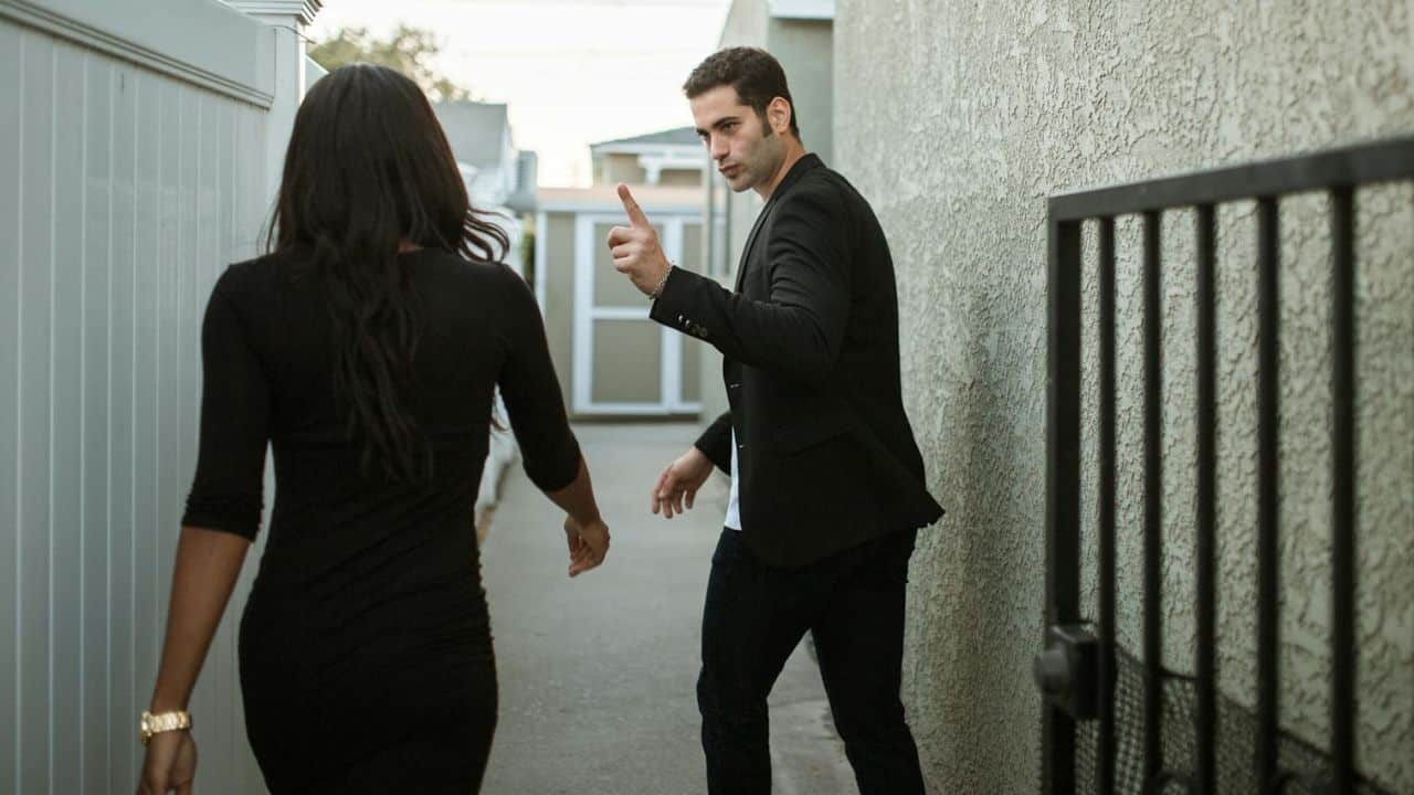 A man points upward while looking toward a woman walking away in an outdoor alley.