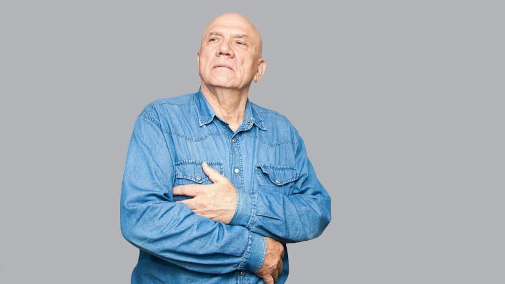A bald man in a denim shirt stands with his arms crossed and looks off-camera.