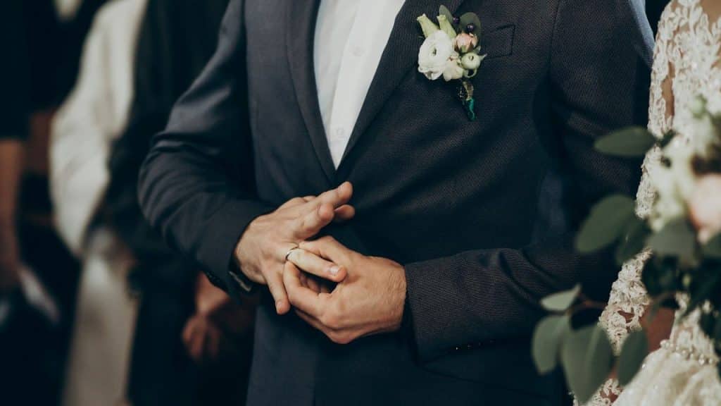 A person in a dark suit adjusts a gold ring on their finger during a ceremony.