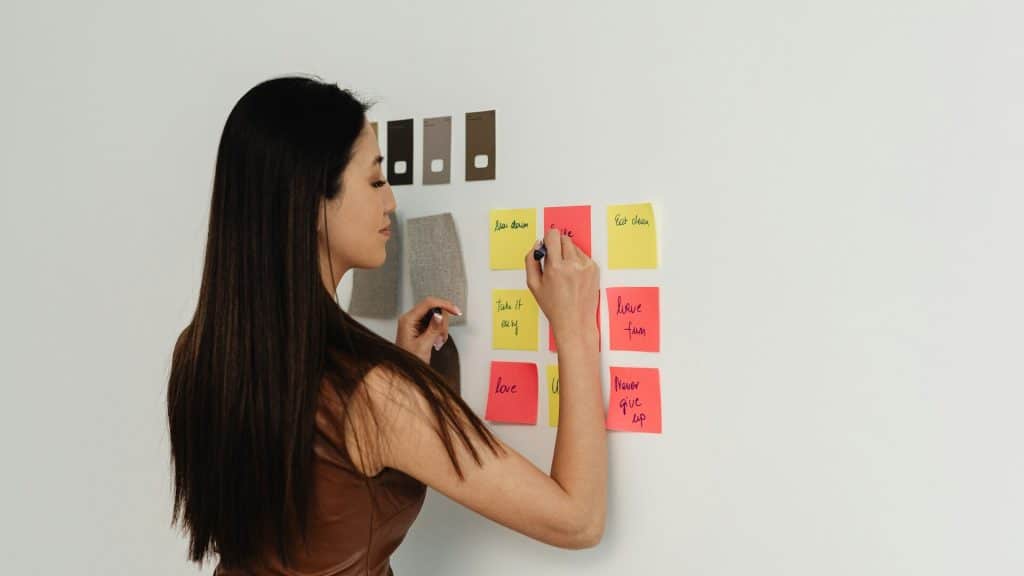 A woman writing notes on a wall with sticky notes.