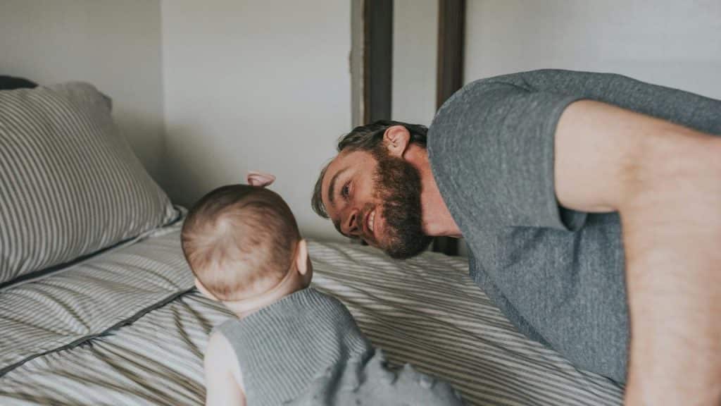 A man lying on a bed facing a baby.