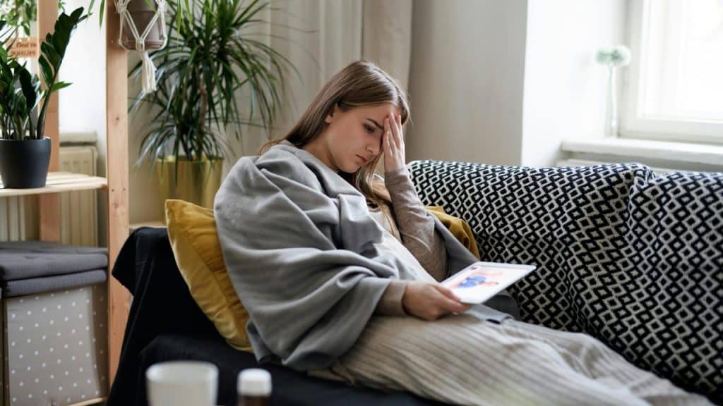 A woman wrapped in a blanket looking at a tablet sadly.