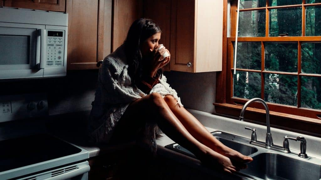 A woman having tea while sitting on a kitchen counter.