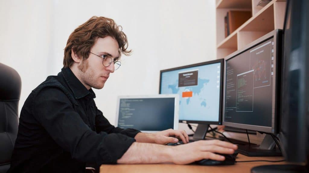 A man works on multiple computer screens at a desk.