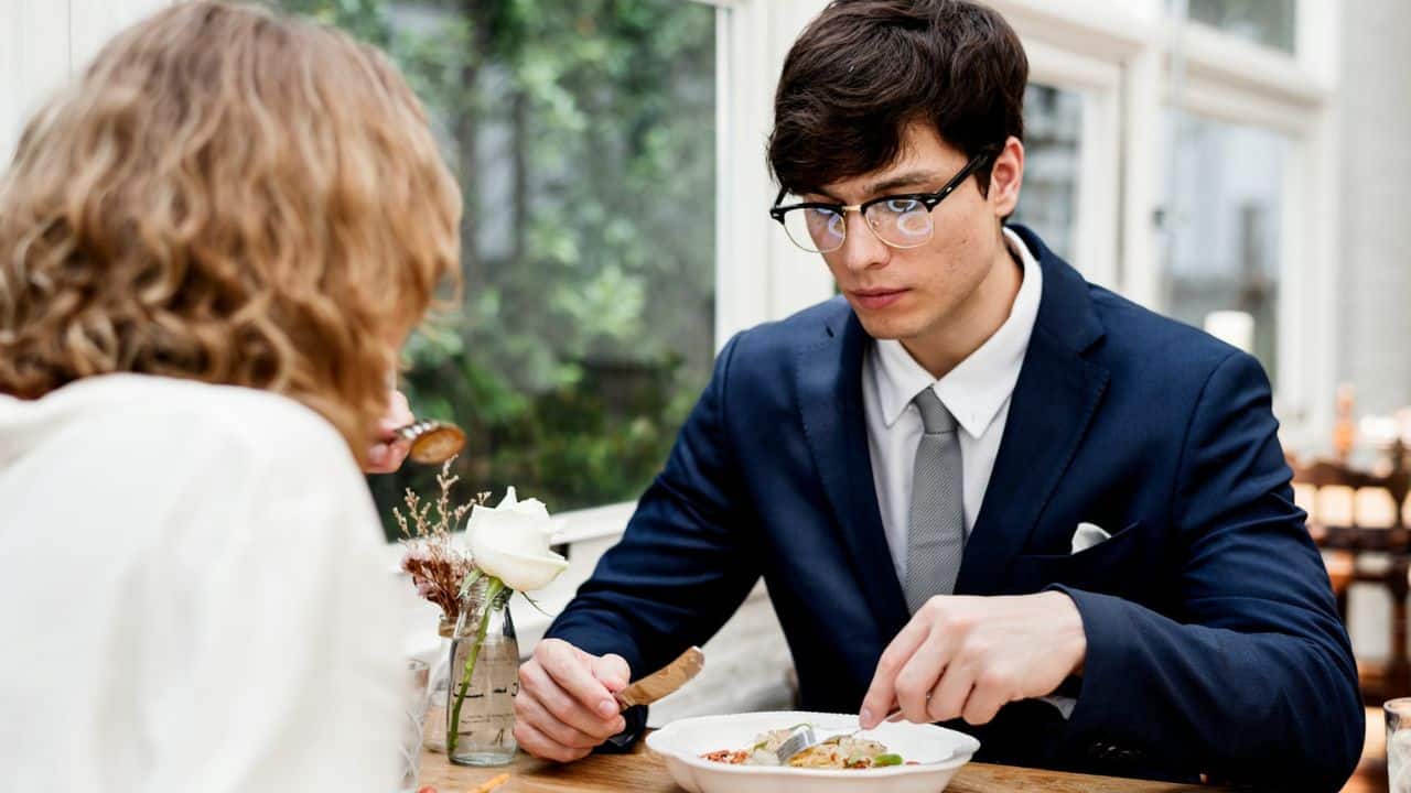 A man in a suit eats a meal while looking down with a serious expression.