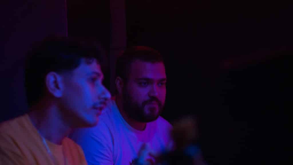 A man talking to another bearded man in a dimly lit room.