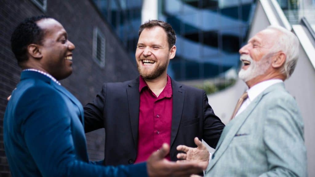 Three men in business attire laughing together outside an office building.
