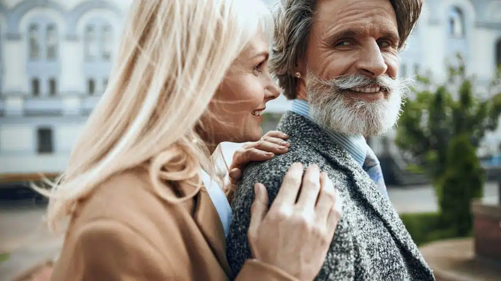A mature man with a white beard and a woman smiling together outdoors.