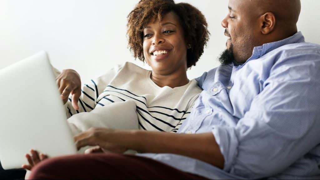 A couple smiling while looking at a laptop.