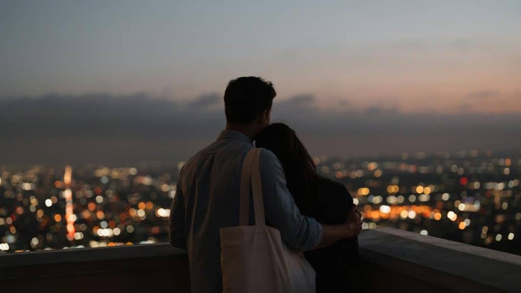A couple standing together at dusk while overlooking a city skyline.