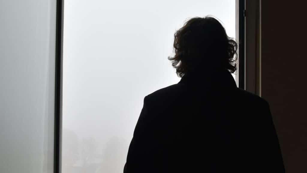 A silhouetted person standing by a window and looking outside.