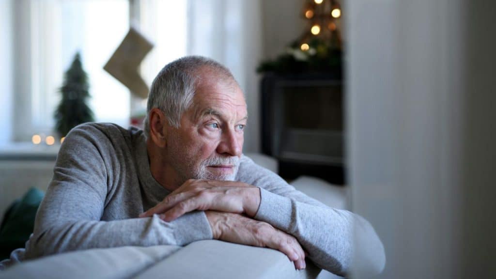 A contemplative senior man leans on a couch, looking into the distance.