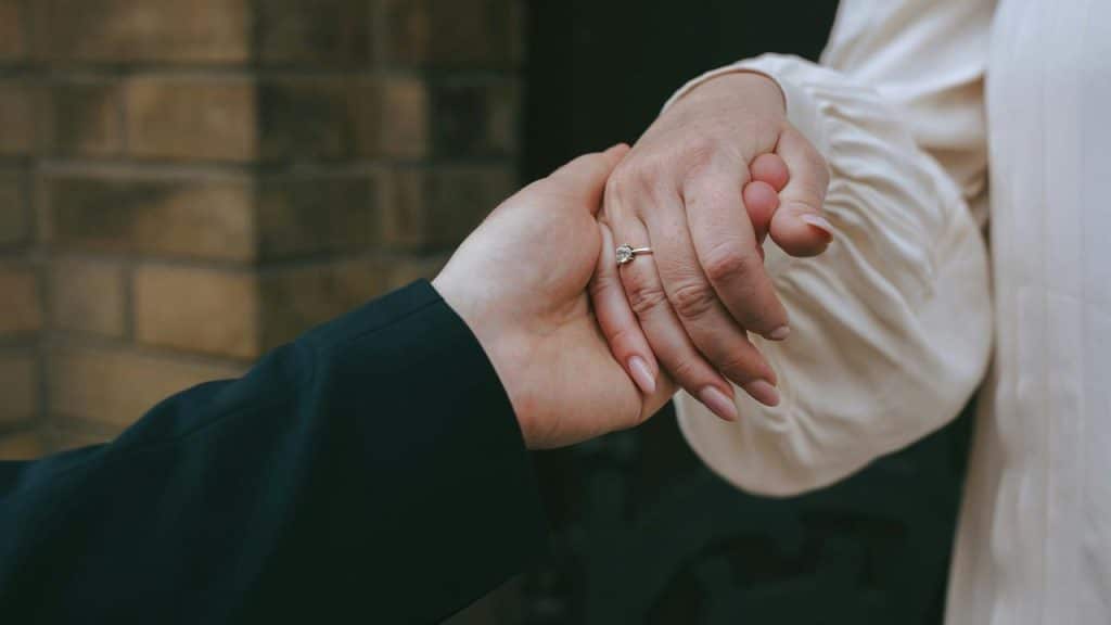 A close-up of two people holding hands, highlighting an engagement ring.