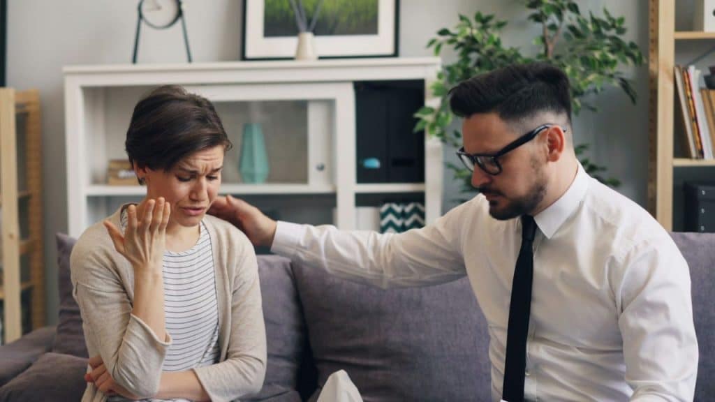 A man in a white shirt and tie places a hand on a distressed woman's shoulder.