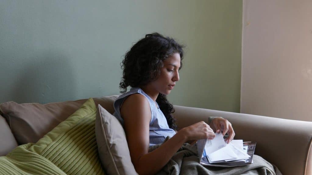A woman sitting on a couch opening and reading mail.