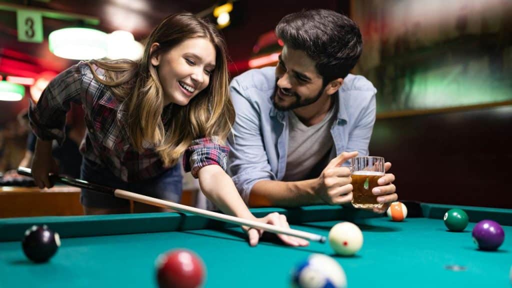 A couple smiling and playing pool together, with one holding a drink.