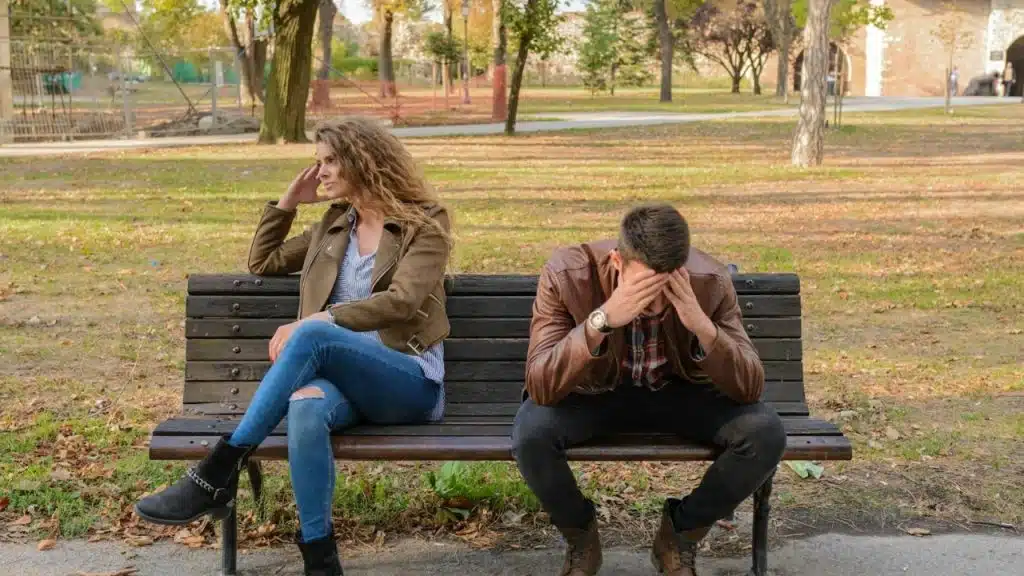 A man and woman sit apart on a park bench looking in opposite directions.
