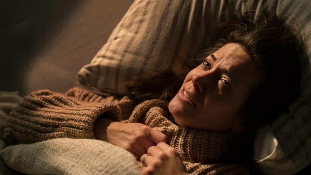 A woman in a thick sweater lies on a pillow, looking upward with a slight smile.