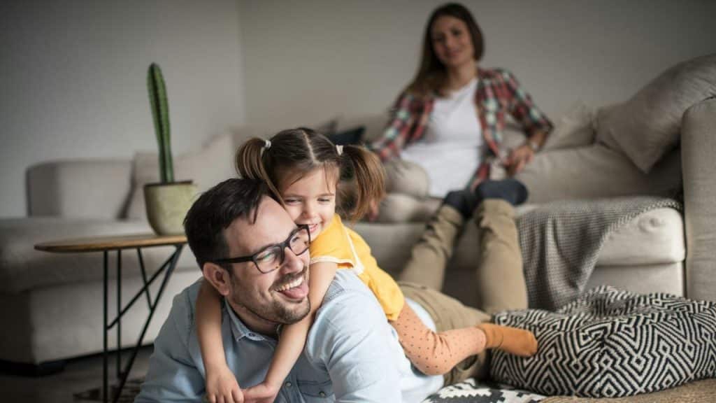 A man lies on a floor with a young child while a woman sits behind.