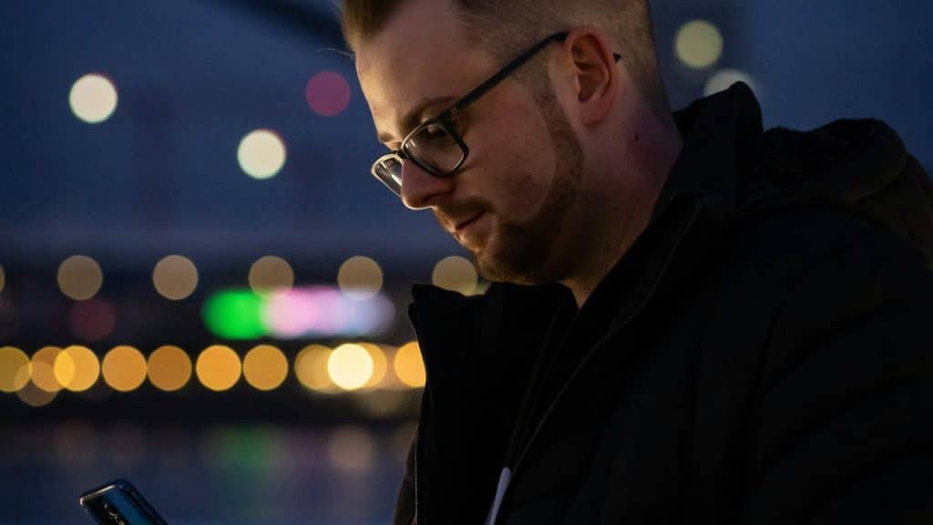 A man wearing glasses looking at his phone at night.