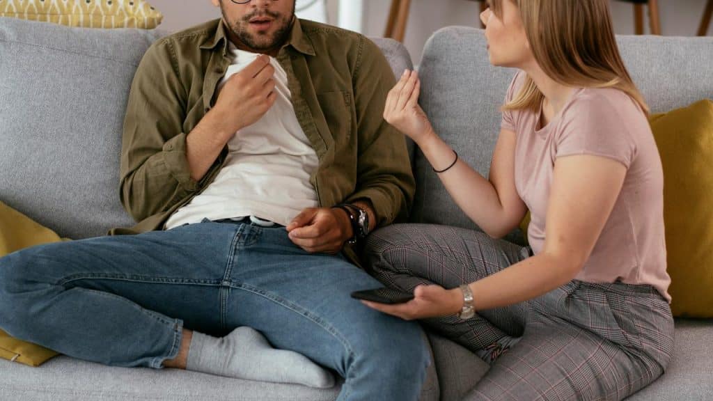 A couple sitting on a couch in a tense conversation, with the woman gesturing.