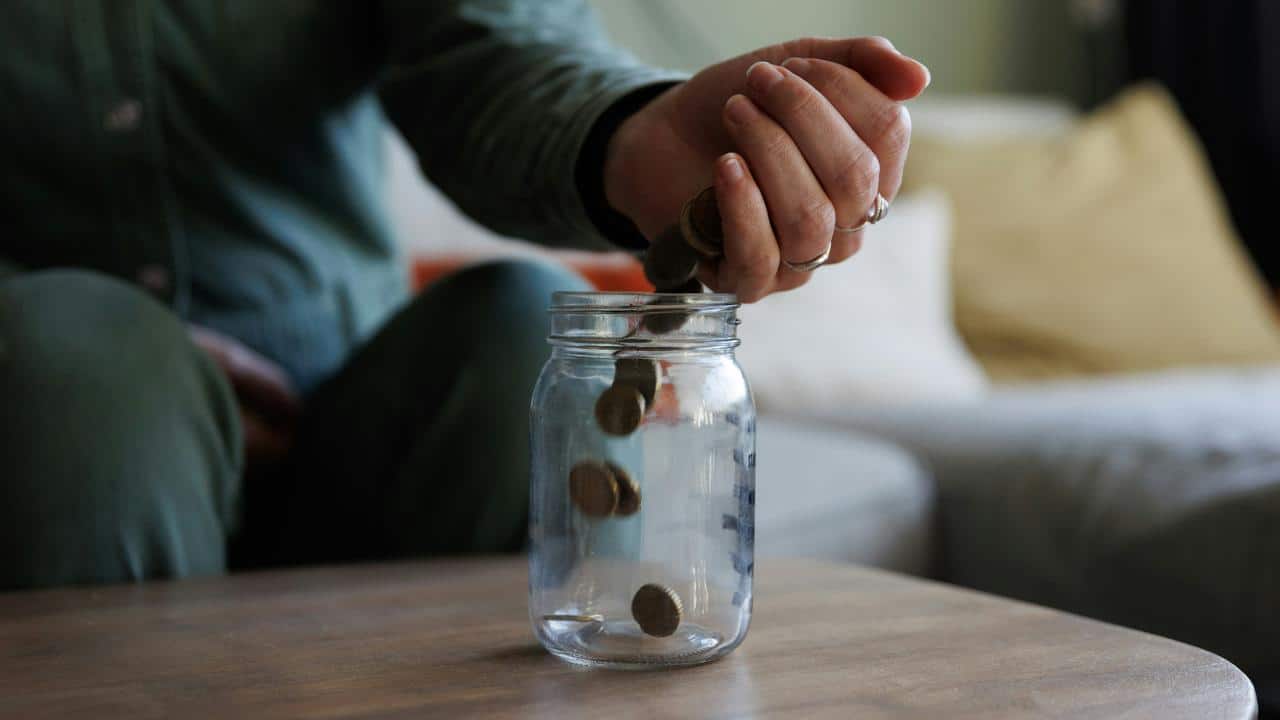 A person dropping coins into a glass jar.