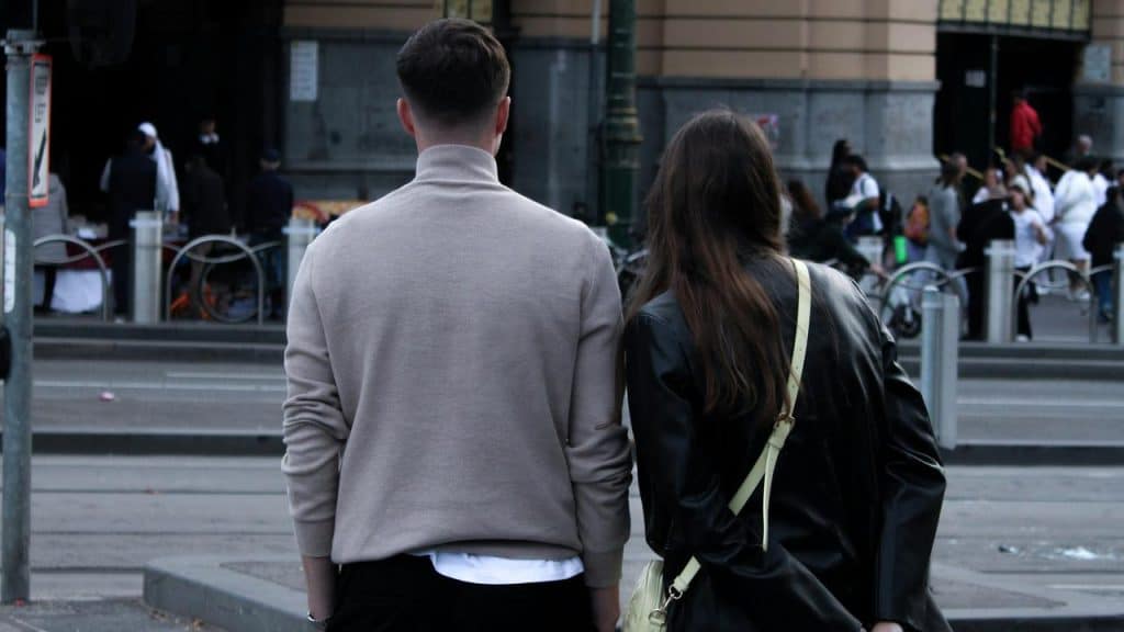 A pair of people seen from behind standing at a city crosswalk.