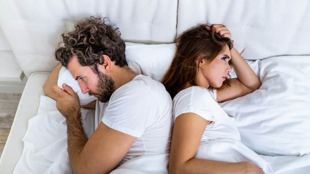 A man and woman lie in bed back-to-back while looking away from each other.