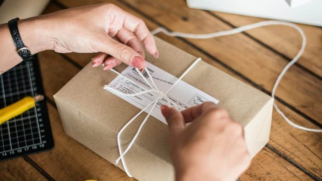 A pair of hands tying string around a small wrapped package.