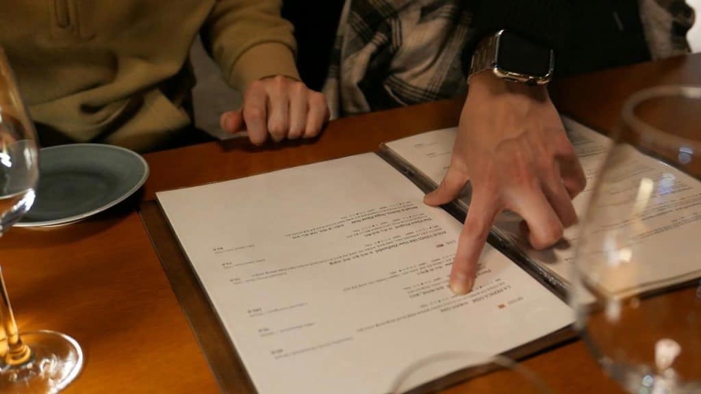 A person pointing at a menu on a table at a restaurant.