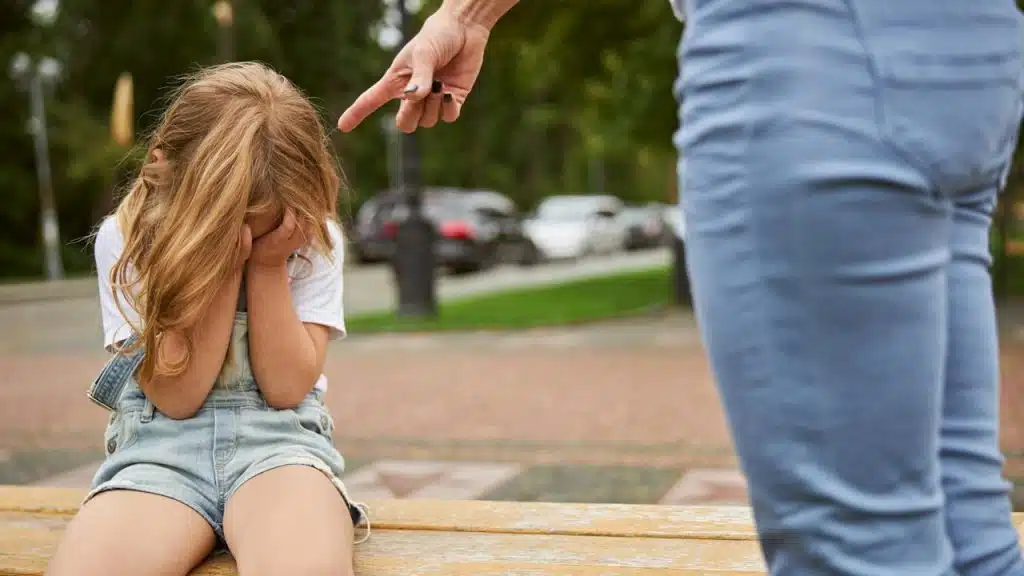 A crying girl holding a hand on her face while sitting on the bench in the city park.