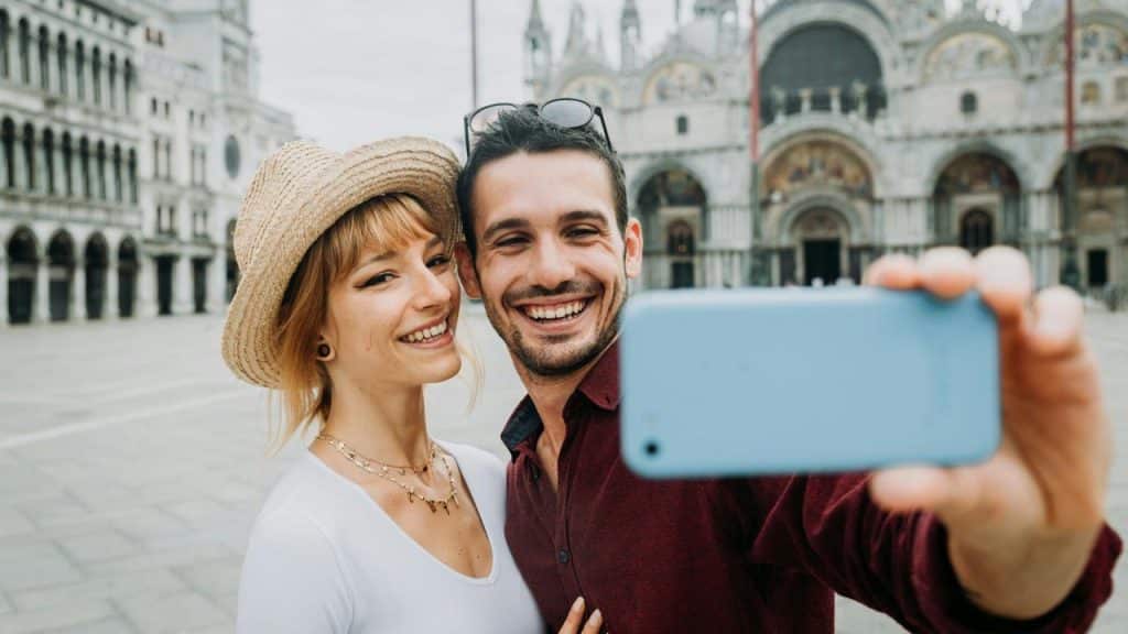 A smiling couple taking a selfie in a large historic square.