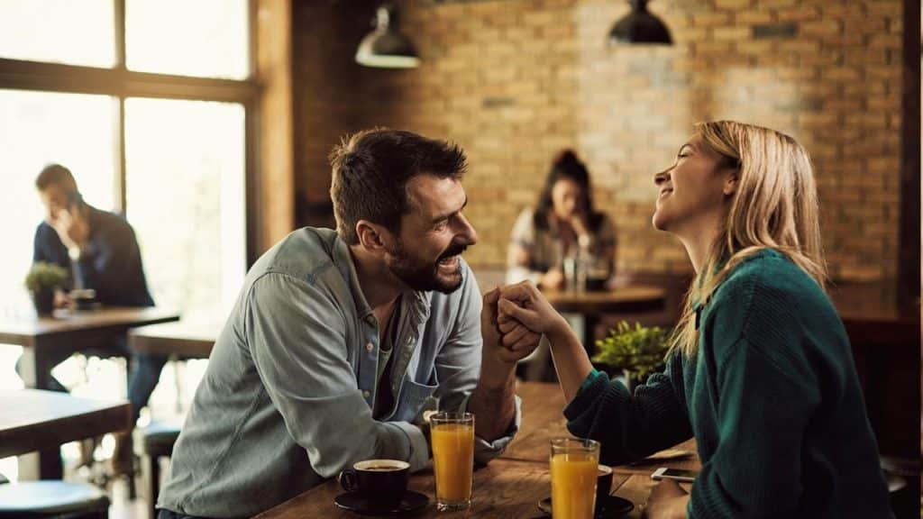 A couple laughing while holding hands at a cafe.