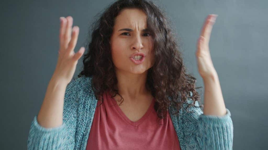 A woman gesturing with raised hands, appearing frustrated or upset.