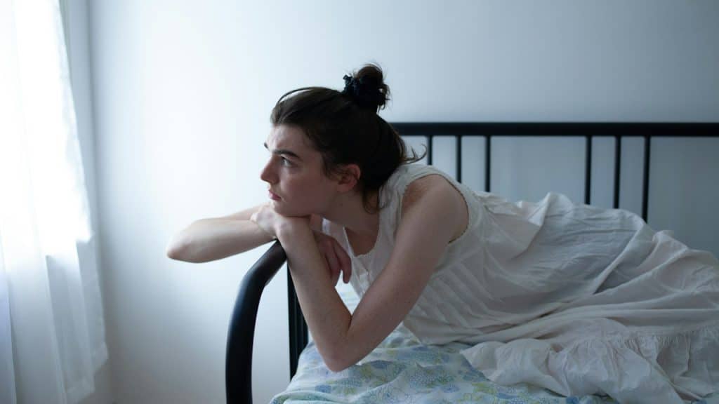 A sad woman resting her head on her hands while leaning on the arm of a couch.