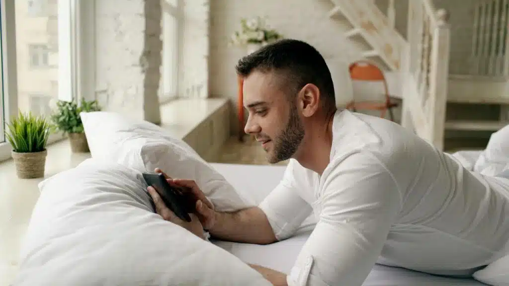 A man lying on a bed using a smartphone.