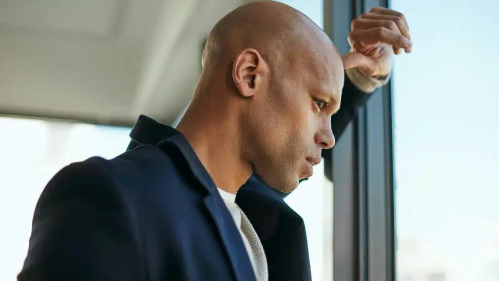 A man leans against a window looking thoughtful.