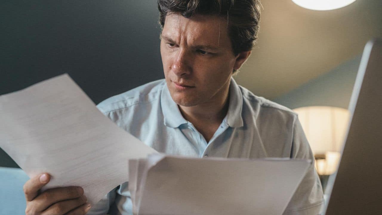 A man in a light blue polo shirt looks intently at papers held in his hands.