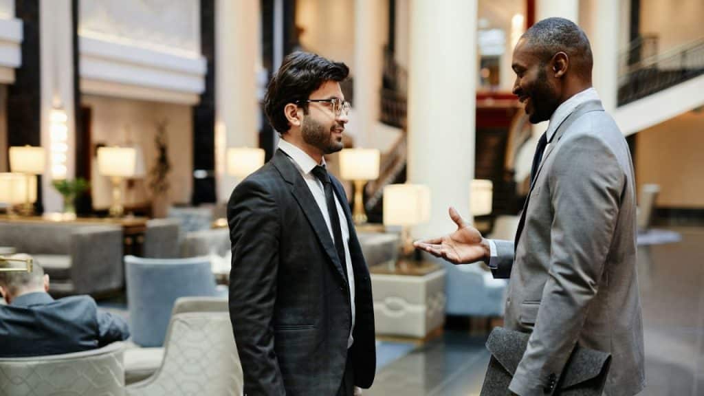Two men in suits stand in a lobby and engage in a conversation.