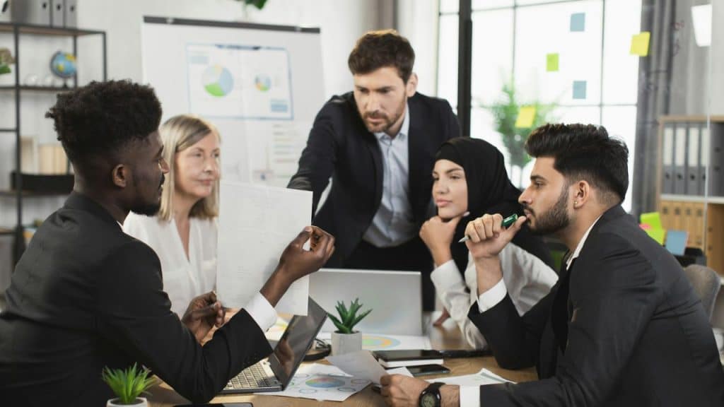 A group of diverse professionals sit around a table looking at a document during a meeting.