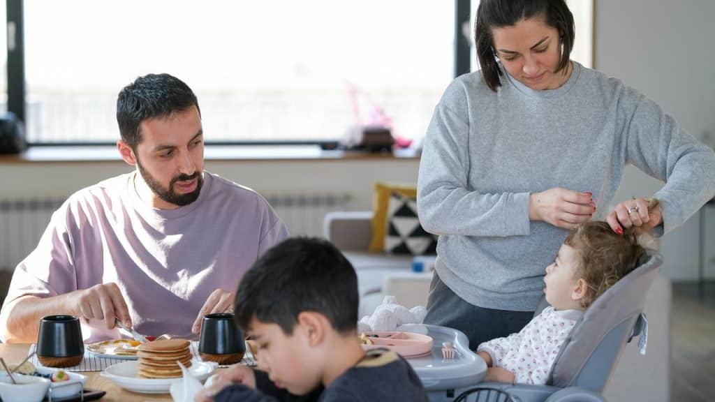 A family eating breakfast as a mother adjusts her toddler’s hair.