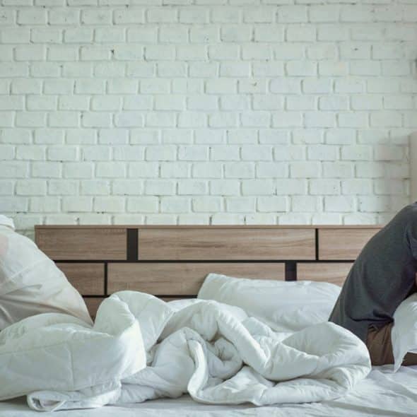 A couple sitting on opposite sides of a bed and not talking to each other.