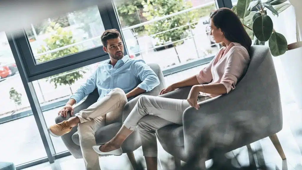 A couple sitting on chairs and talking to each other about something serious.