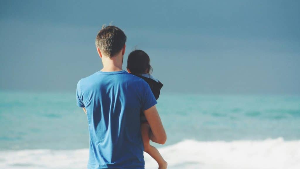 A father holding his child while looking at the ocean.