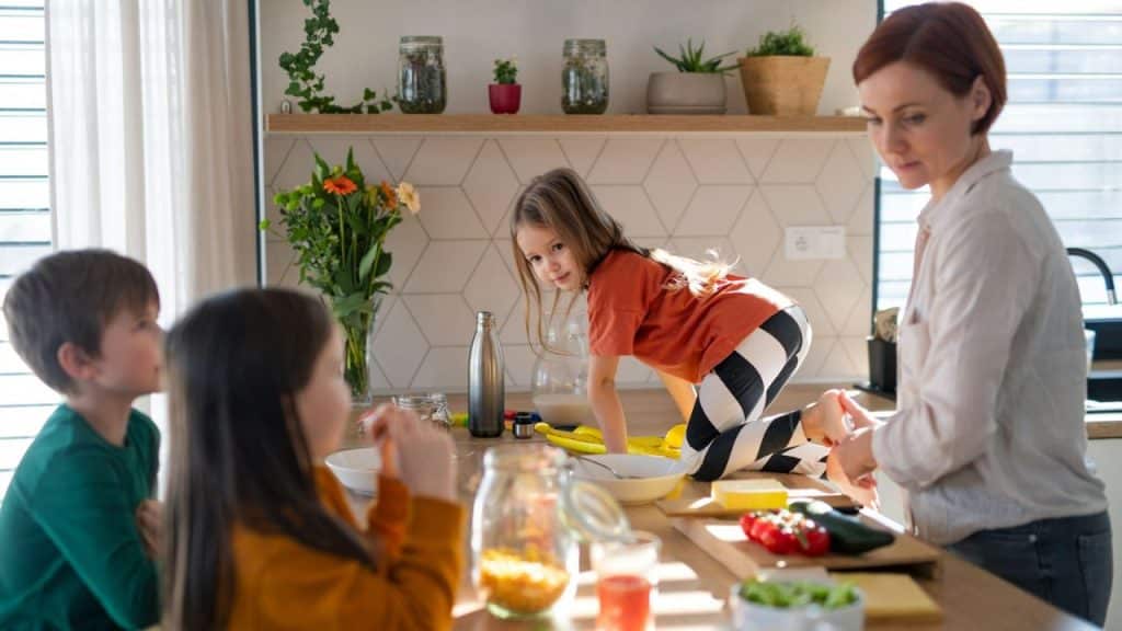 A woman and three young children are in a bright, modern kitchen.