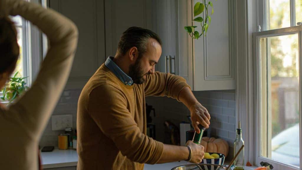 A man prepares food in a kitchen by the window.