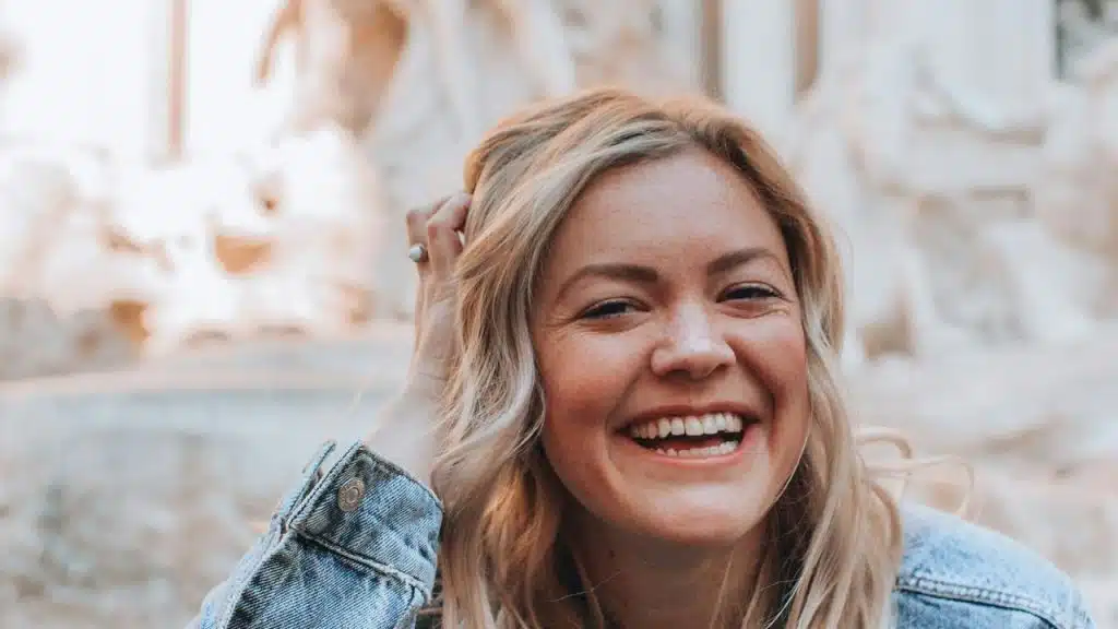 A smiling woman with blonde hair wearing a denim jacket outdoors.