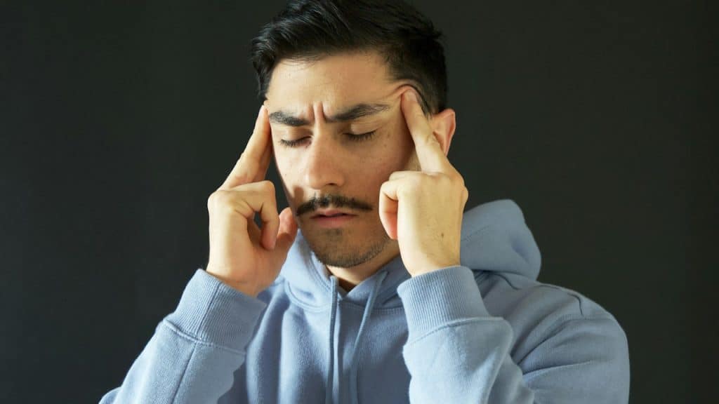 A mustached man with closed eyes massaging his temples and looking upset.