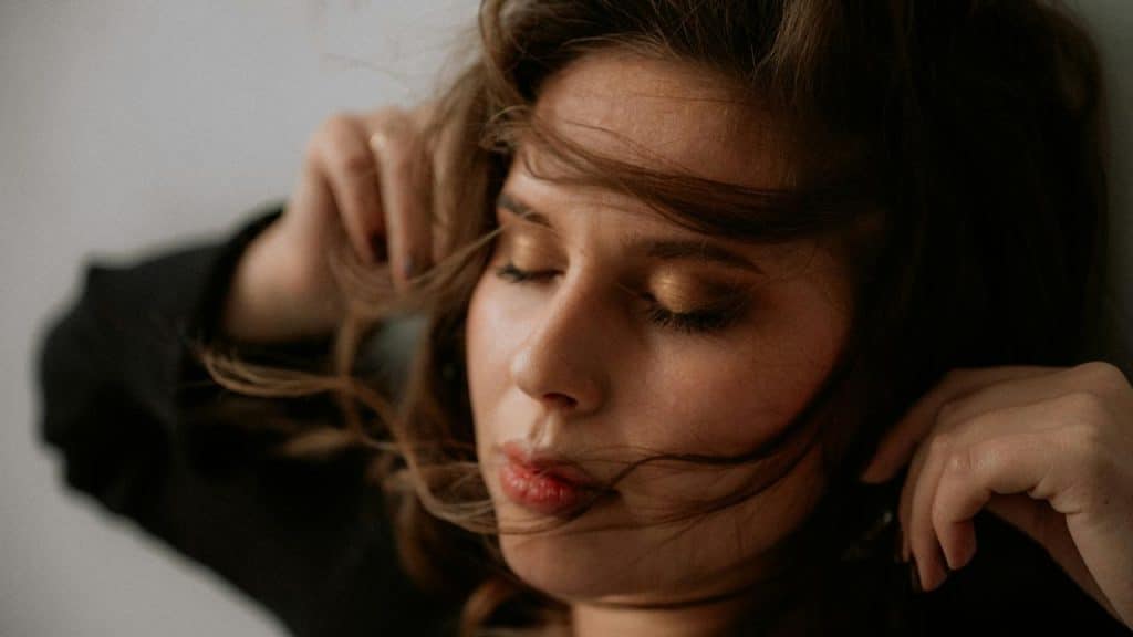 A woman with closed eyes as her hair moves softly across her face.