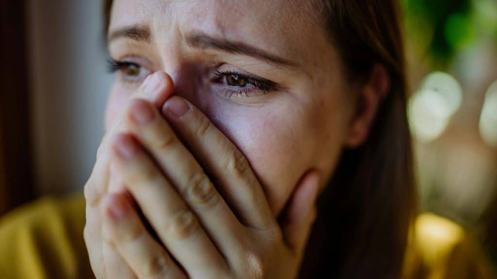 A woman covering her mouth with her hands, looking sad.